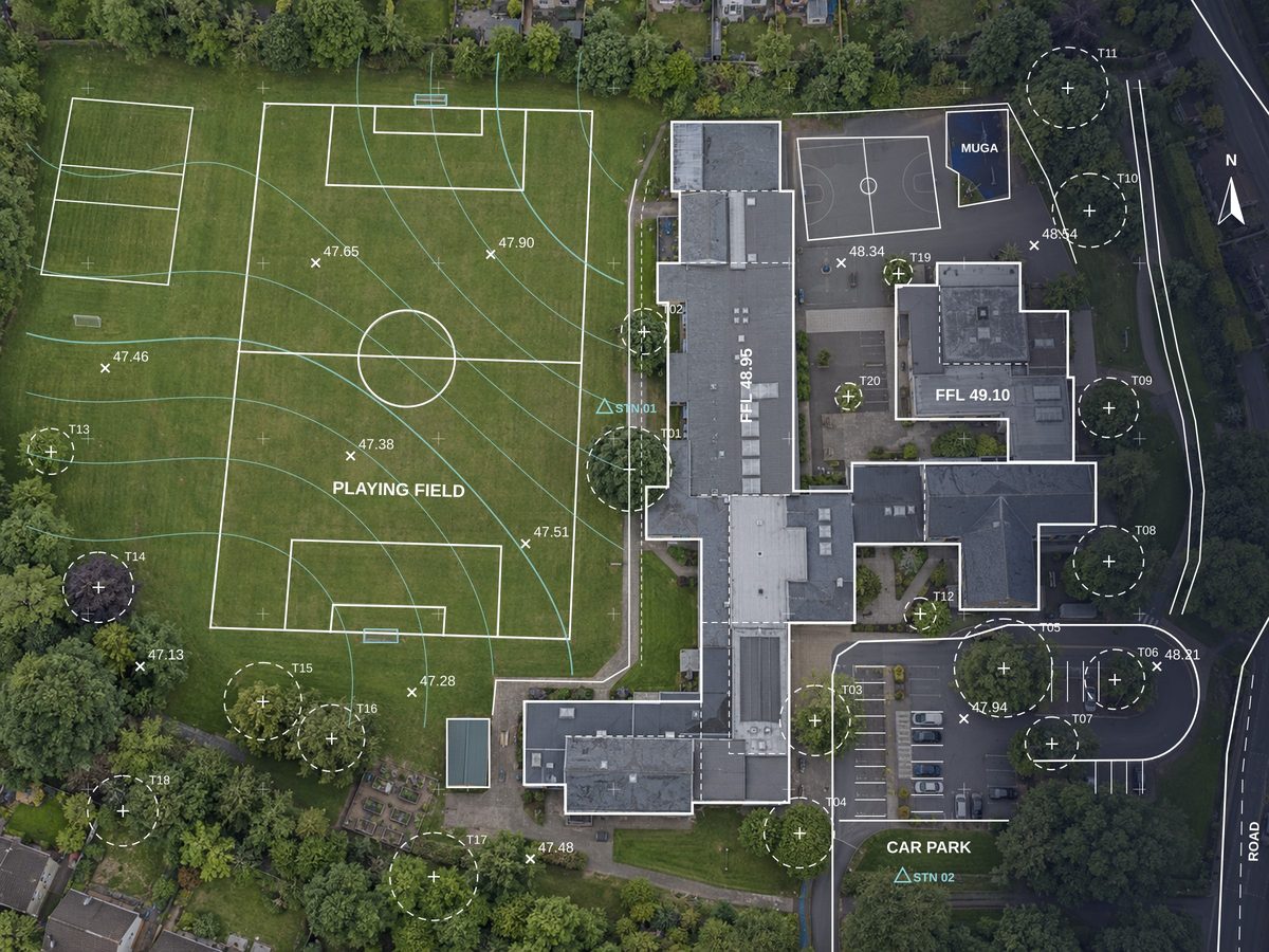 Drone orthophoto of a school site with topographical survey linework overlaid: buildings, pitches, car park, paths, trees, levels and contours