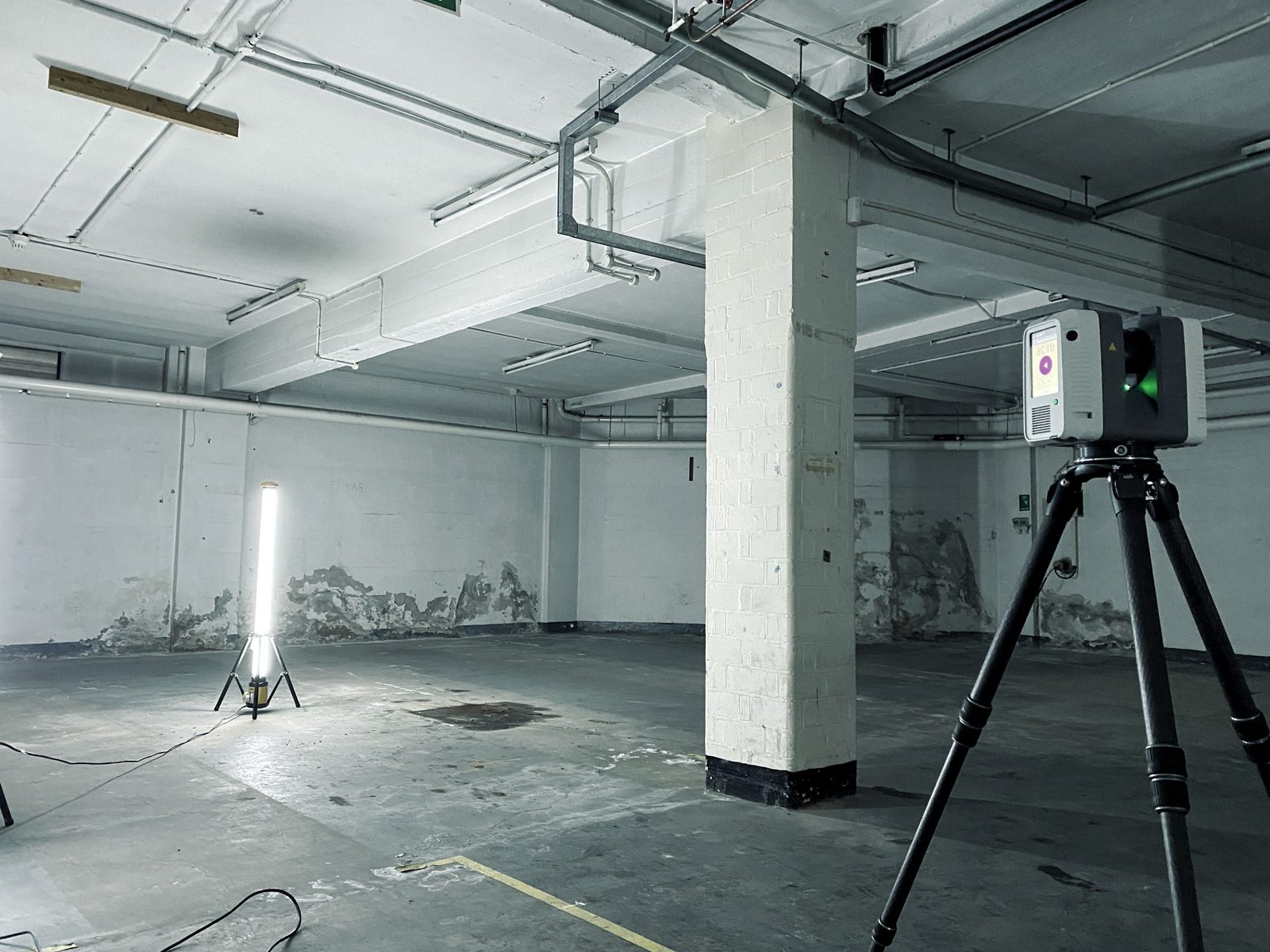 Laser scanner on a tripod capturing a stripped-out basement level with exposed services