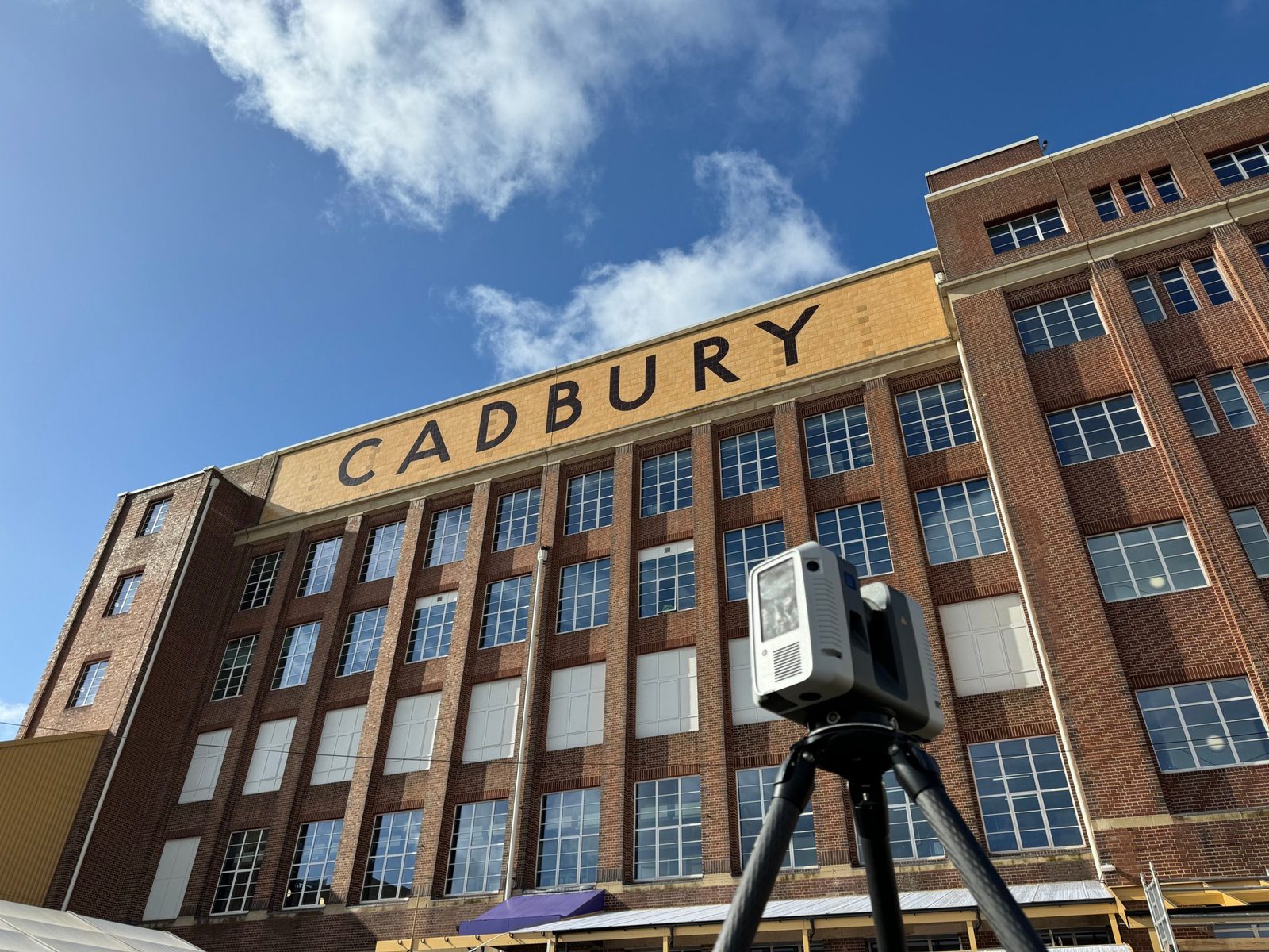 Leica laser scanner on a tripod in front of a large brick factory building
