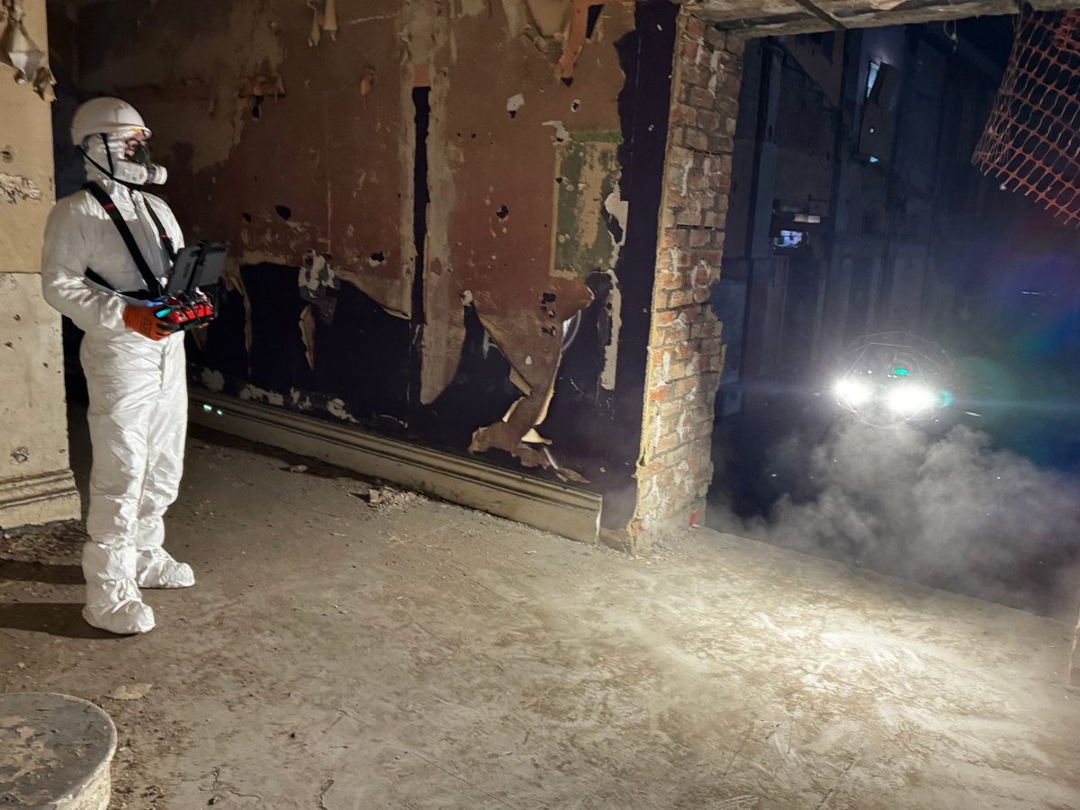 Spacion pilot in protective equipment flying a caged inspection drone through a derelict building interior
